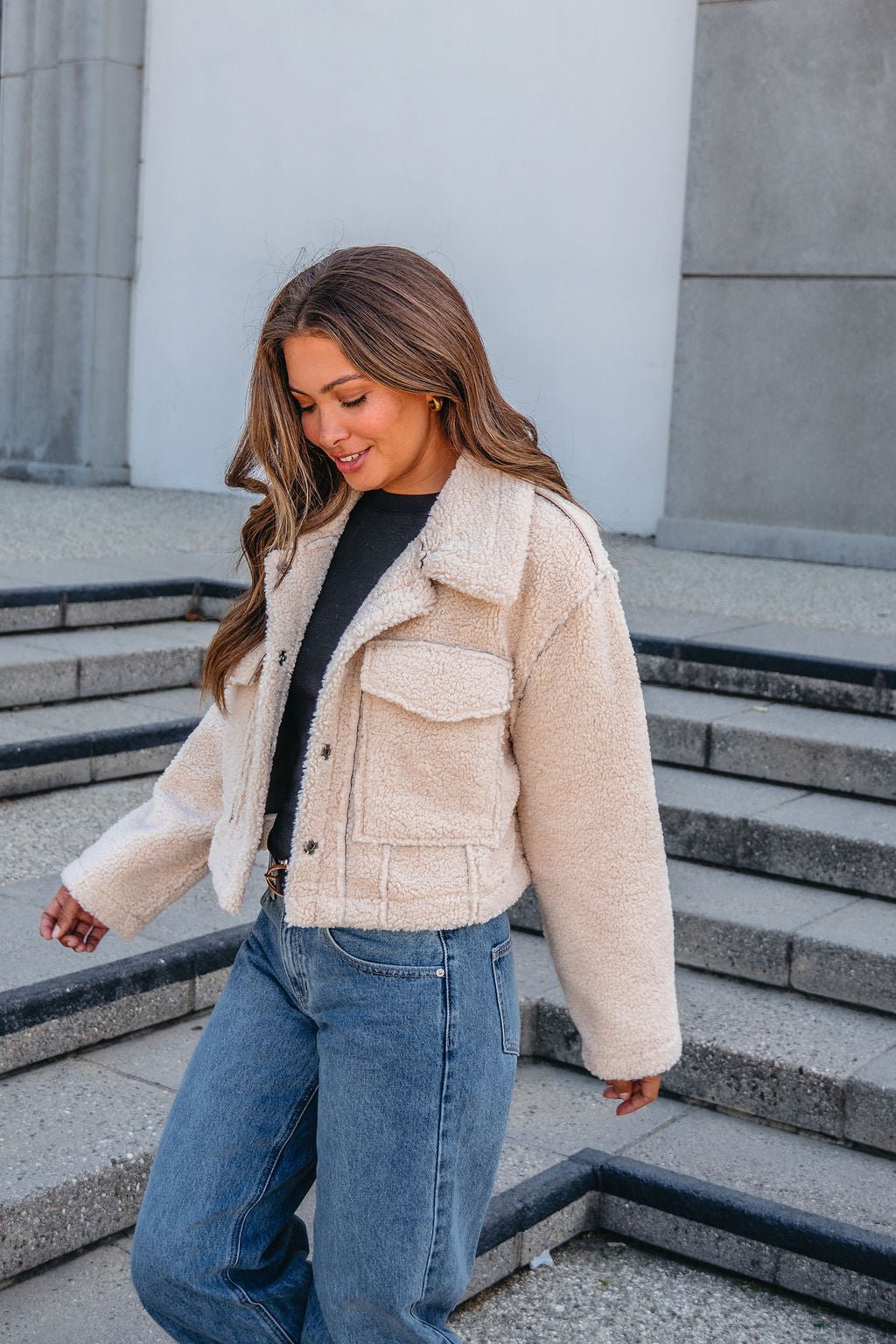 A woman in a Brown Mix Reversible Suede Sherpa Jacket and blue jeans walks down steps, smiling—perfect for fall.