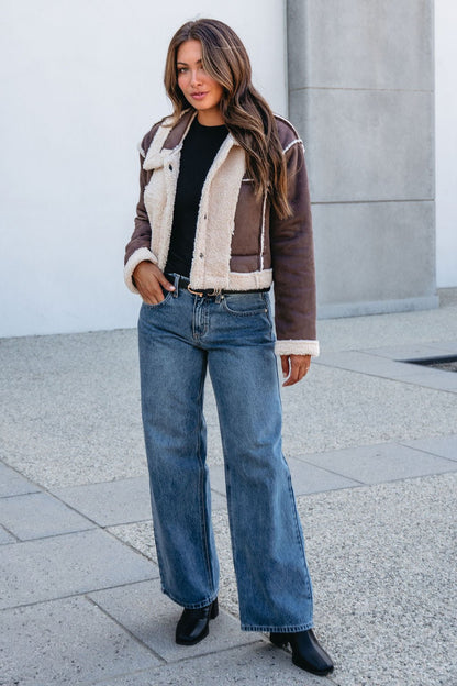 Woman in a Brown Mix Reversible Suede Sherpa Jacket, black shirt, wide-leg jeans, and boots—her fall outfit essential.