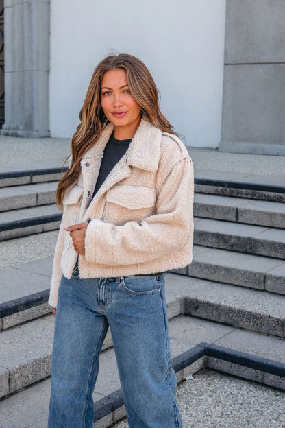 A woman wears a Brown Mix Reversible Suede Sherpa Jacket and blue jeans, standing outdoors on stone steps, smiling at the camera.