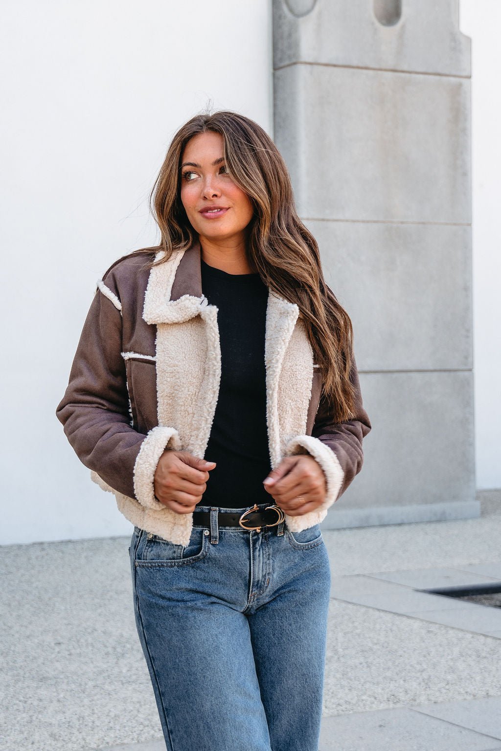 Woman in a Brown Mix Reversible Suede Sherpa Jacket, black top, and blue jeans—a cozy must-have for chilly fall days.
