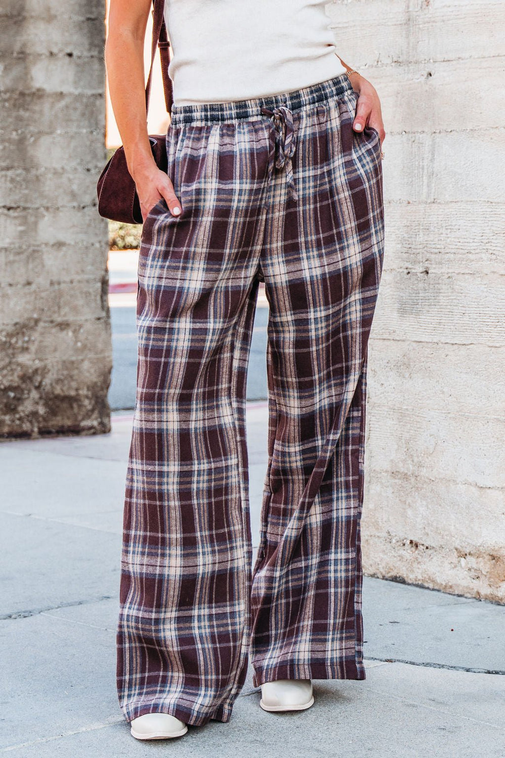 Model wears Brown Plaid Wide Leg Pants - FINAL SALE with a white top and shoes, standing by a concrete wall.