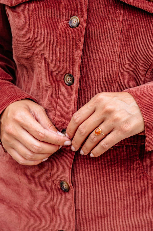 A person in a red corduroy jacket buttons up, showcasing the Brown Resin Acrylic Band Statement Ring - DOORBUSTER.
