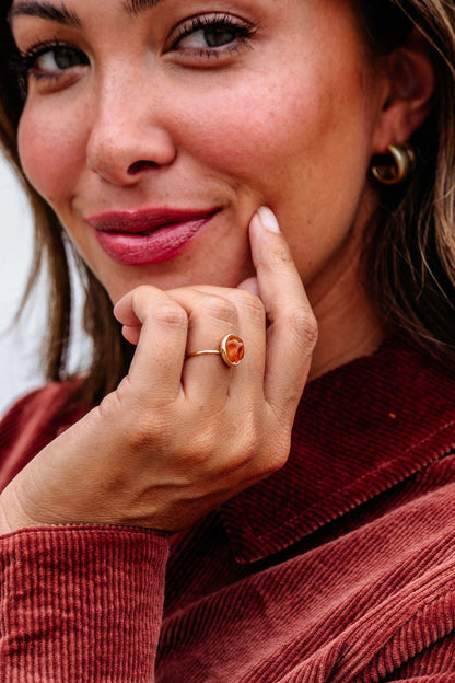 A brown-haired woman touches her face, wearing the Brown Resin Acrylic Band Statement Ring - DOORBUSTER and a red corduroy jacket.