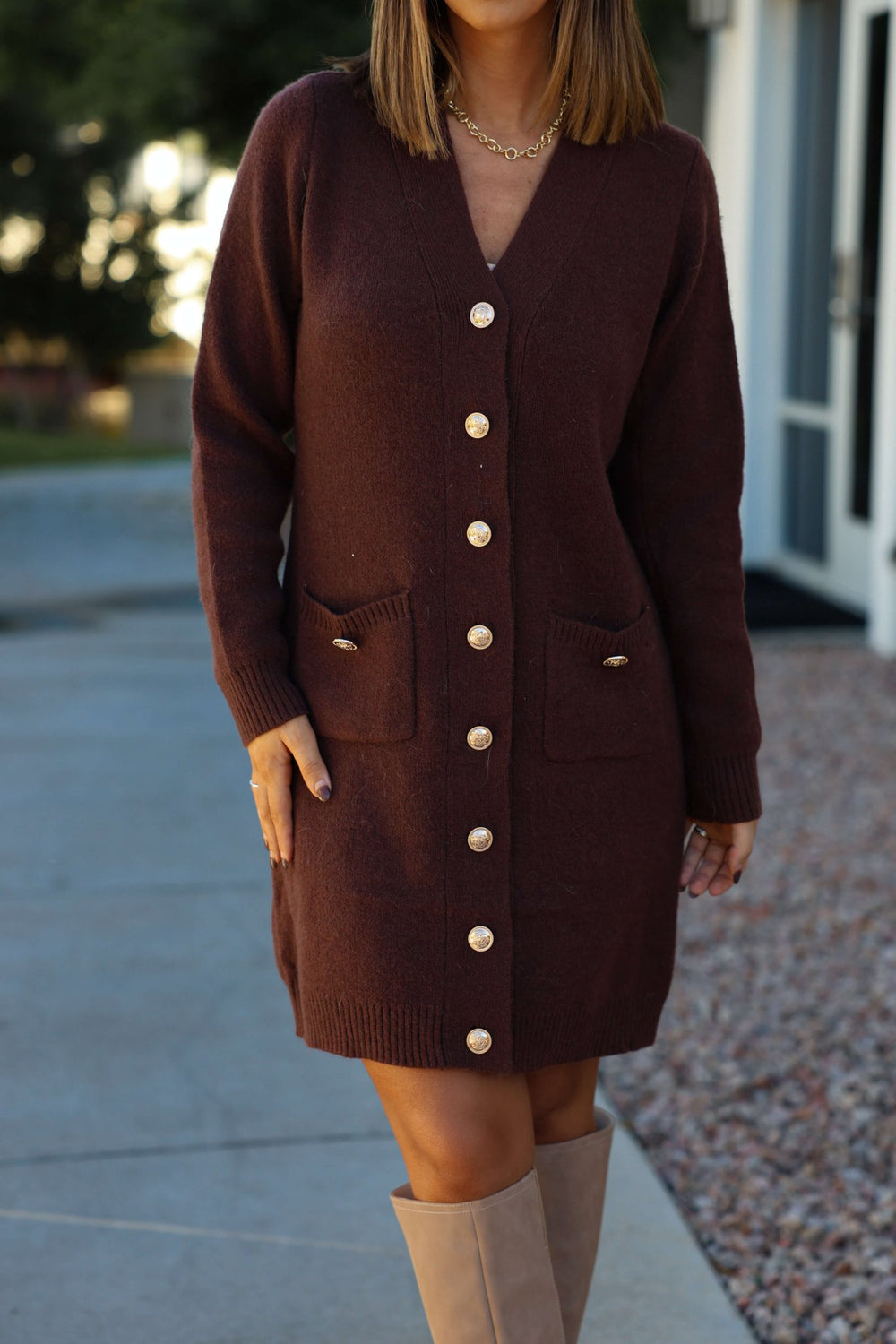 A woman wearing the Brown Ribbed Cardigan Sweater Dress, featuring gold buttons and pockets, with tan knee-high boots.