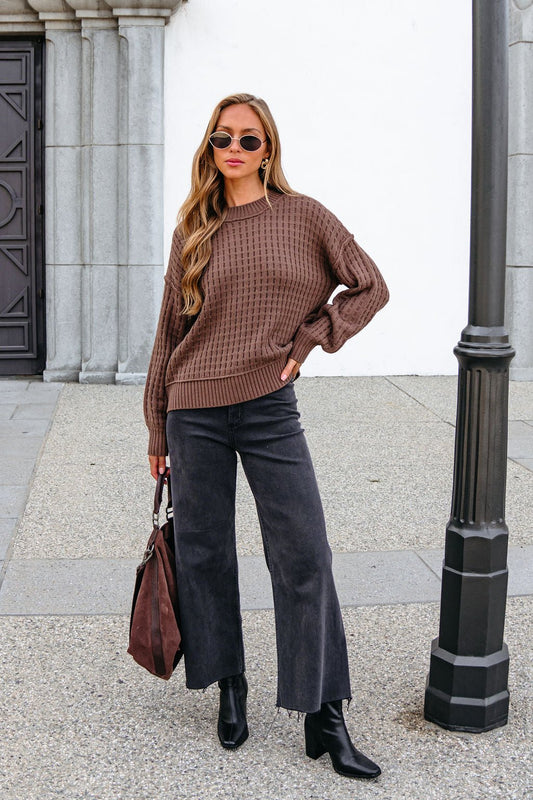 Woman in a Brown Waffle Knit Sweater, black jeans, and boots holds a brown bag by a lamppost, radiating effortless cool.