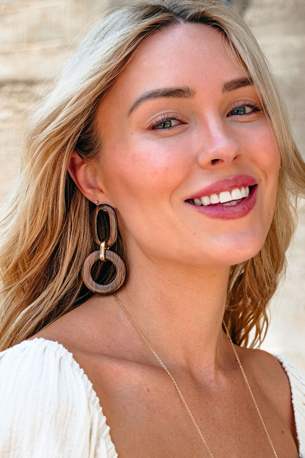 Smiling woman in white top models Brown Wooden Linked Dangle Earrings against a neutral background.
