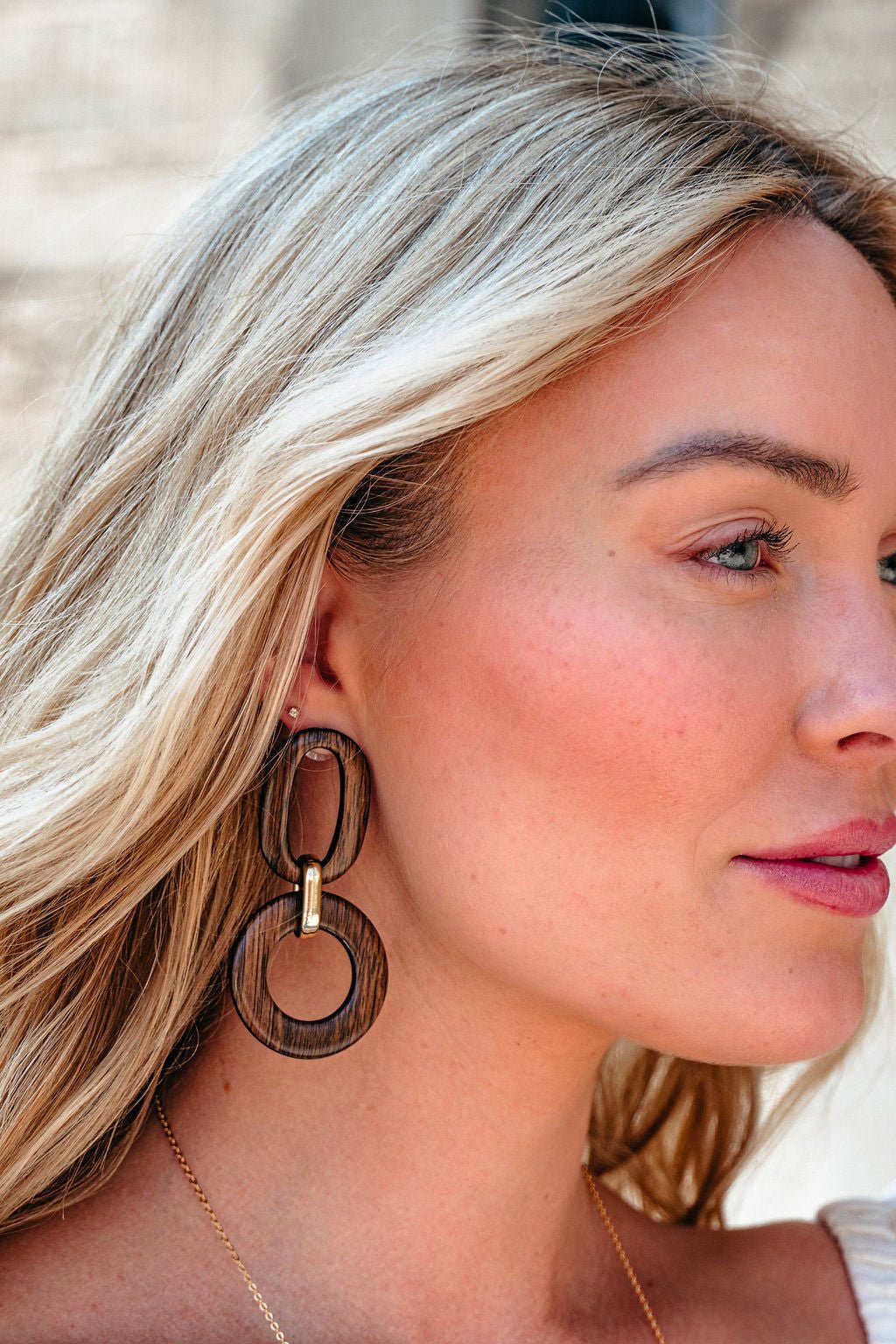 Close-up of a blonde woman wearing Brown Wooden Linked Dangle Earrings in soft natural lighting—an eye-catching accessory.