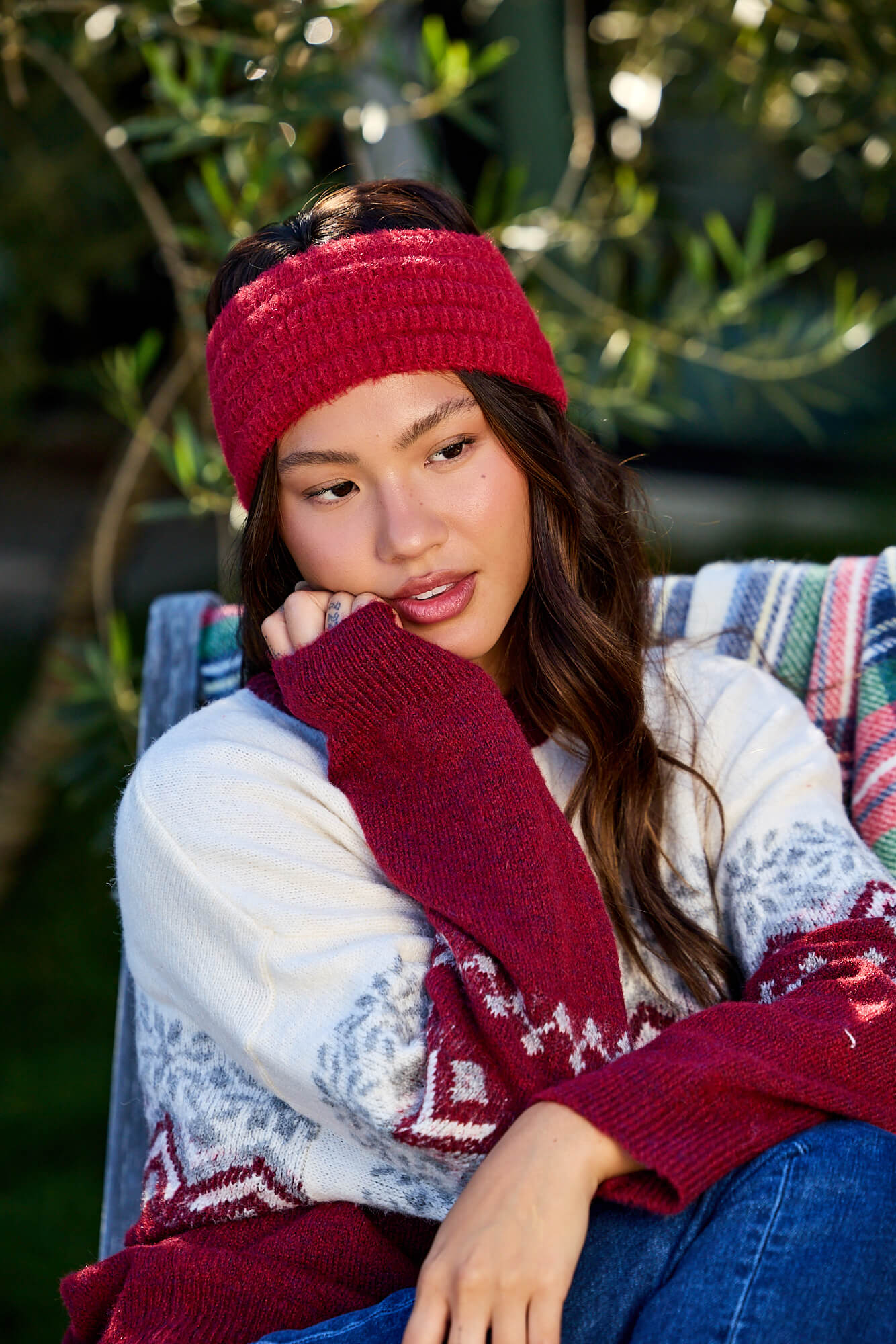 Woman wearing a Burgundy Fuzzy Soft Cable Knit Headband sits outdoors on a striped blanket, looking thoughtful.