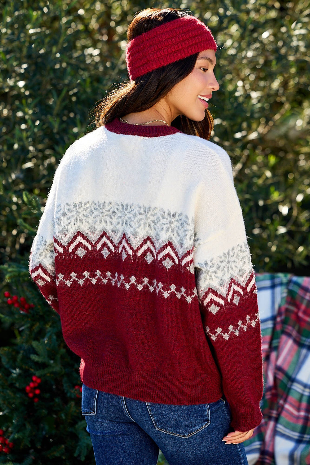 Woman outdoors in a Burgundy Mix Fair Isle Sweater and red headband by greenery—perfect winter outfit inspiration.
