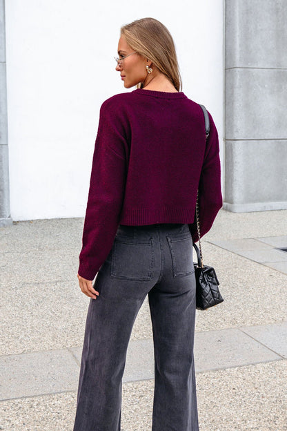 Woman with long hair in a Burgundy Ribbed Button Down Cardigan and gray jeans stands outdoors, wearing sunglasses, facing away.