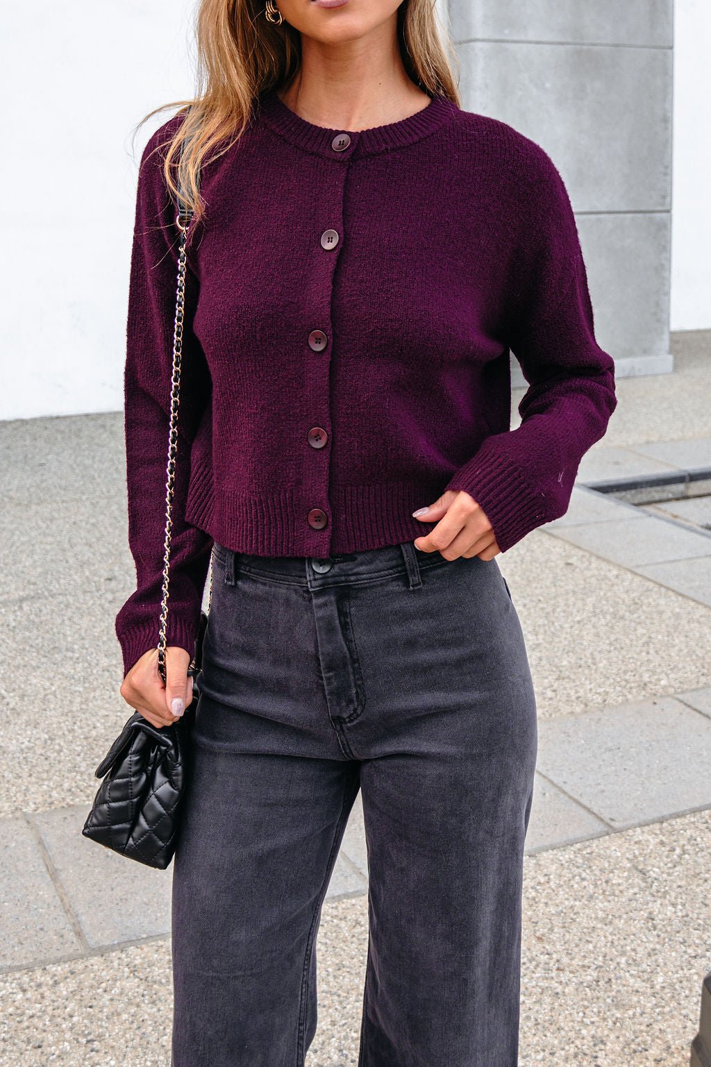 Woman in a burgundy ribbed button down cardigan, black jeans, and a small black chain strap purse.