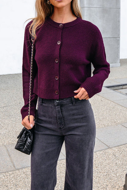 Woman in a burgundy ribbed button down cardigan, black jeans, and a small black chain strap purse.