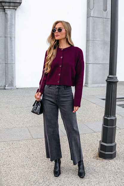 Woman in a Burgundy Ribbed Button Down Cardigan, gray jeans, and black boots stands near a lamp post with a black bag.