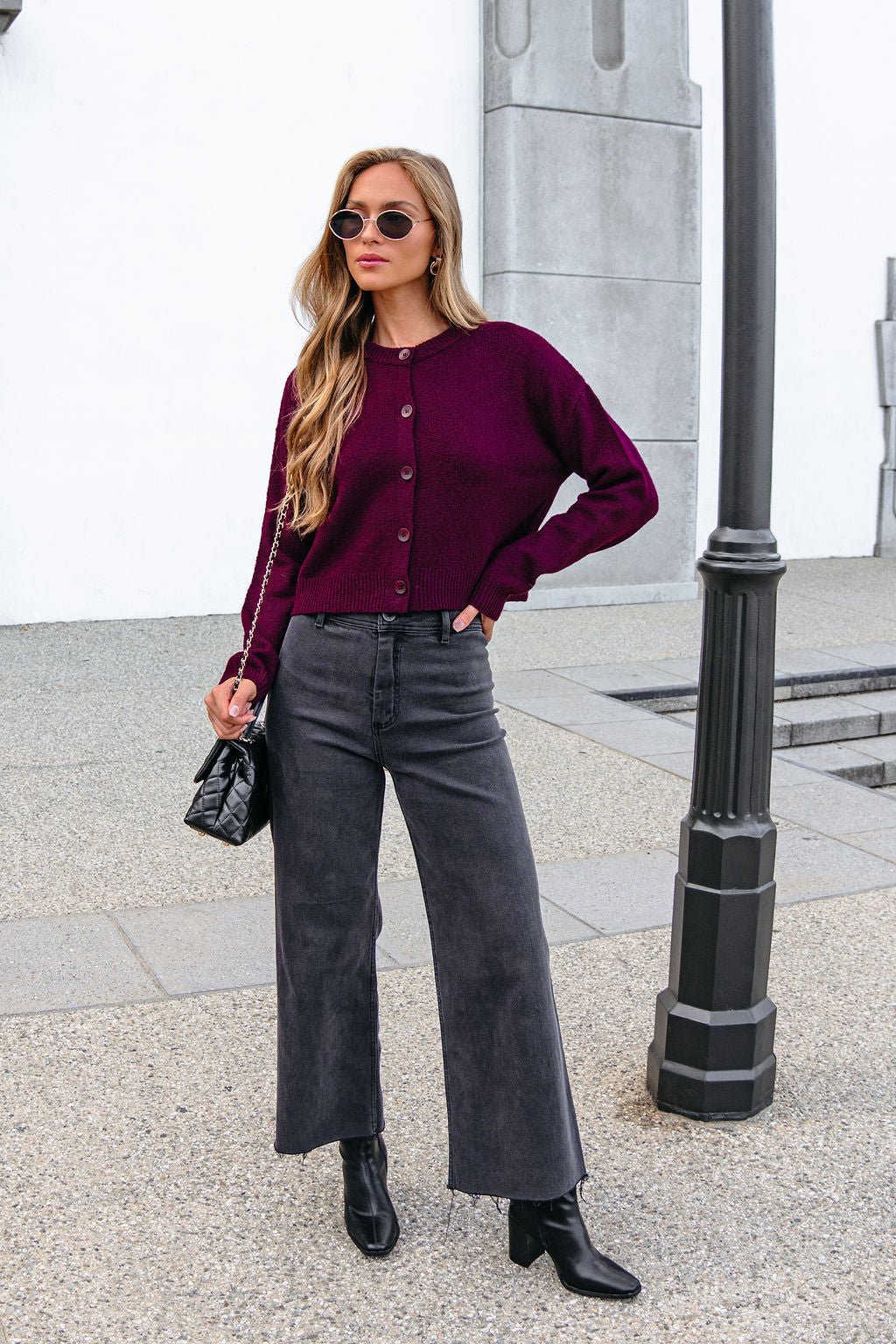 Woman in sunglasses wears a Burgundy Ribbed Button Down Cardigan, black jeans, and boots while standing by a lamppost outdoors.