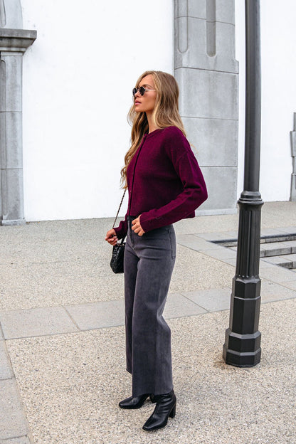 Woman wearing sunglasses, Burgundy Ribbed Button Down Cardigan, gray pants, and black boots stands by a streetlamp on a stone sidewalk.