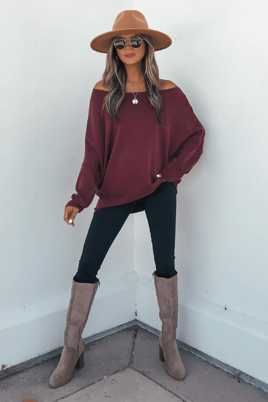 Woman in a tan hat, sunglasses, and Burgundy Soft Cloud Scuba Pullover poses by a white wall in black pants and taupe boots.