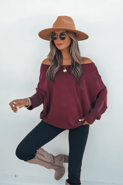 Woman in sunglasses, Burgundy Soft Cloud Scuba Pullover, black pants, taupe boots poses stylishly against a white background.