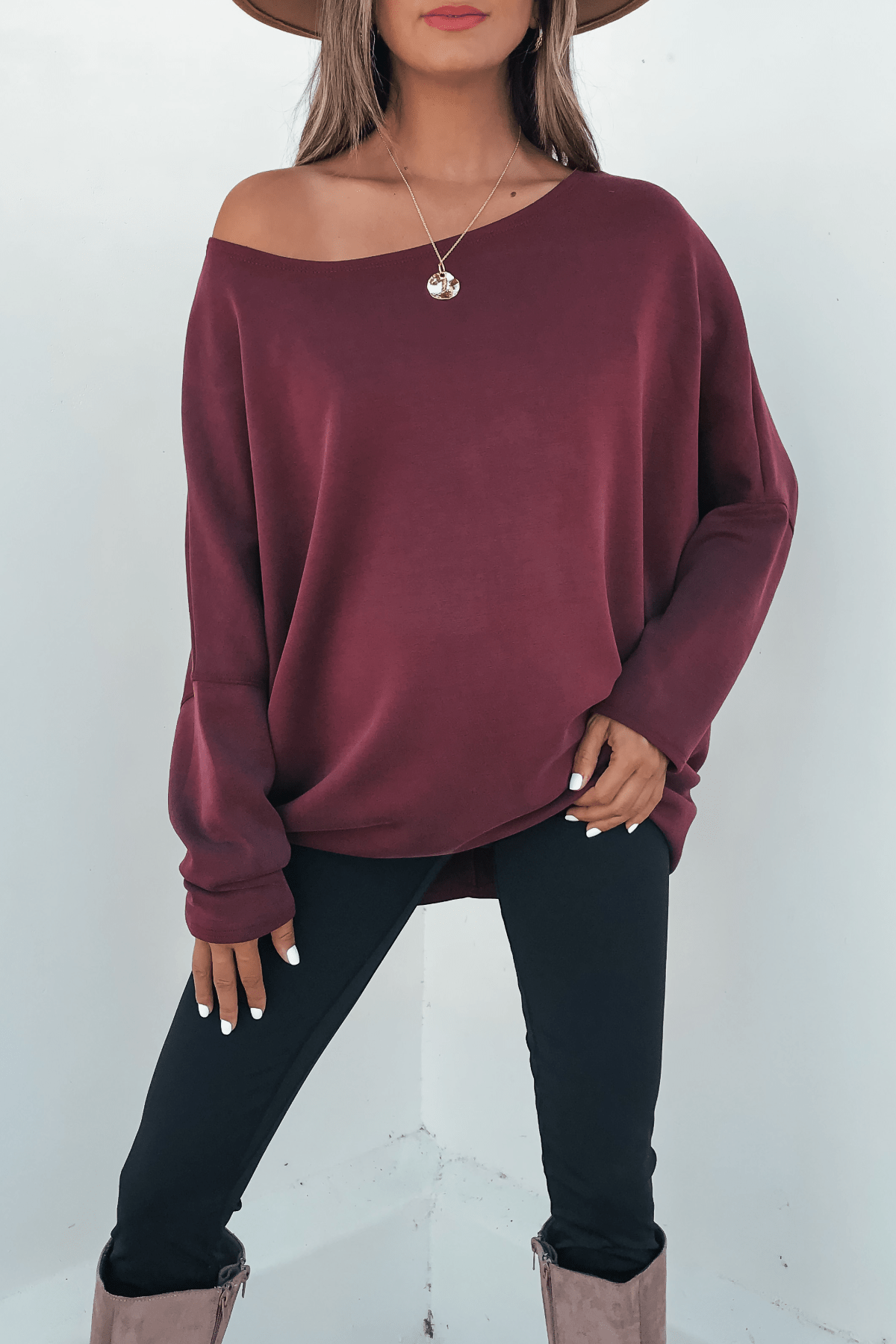 Woman wearing a Burgundy Soft Cloud Scuba Pullover, black pants, taupe boots, brown hat, and round pendant necklace.
