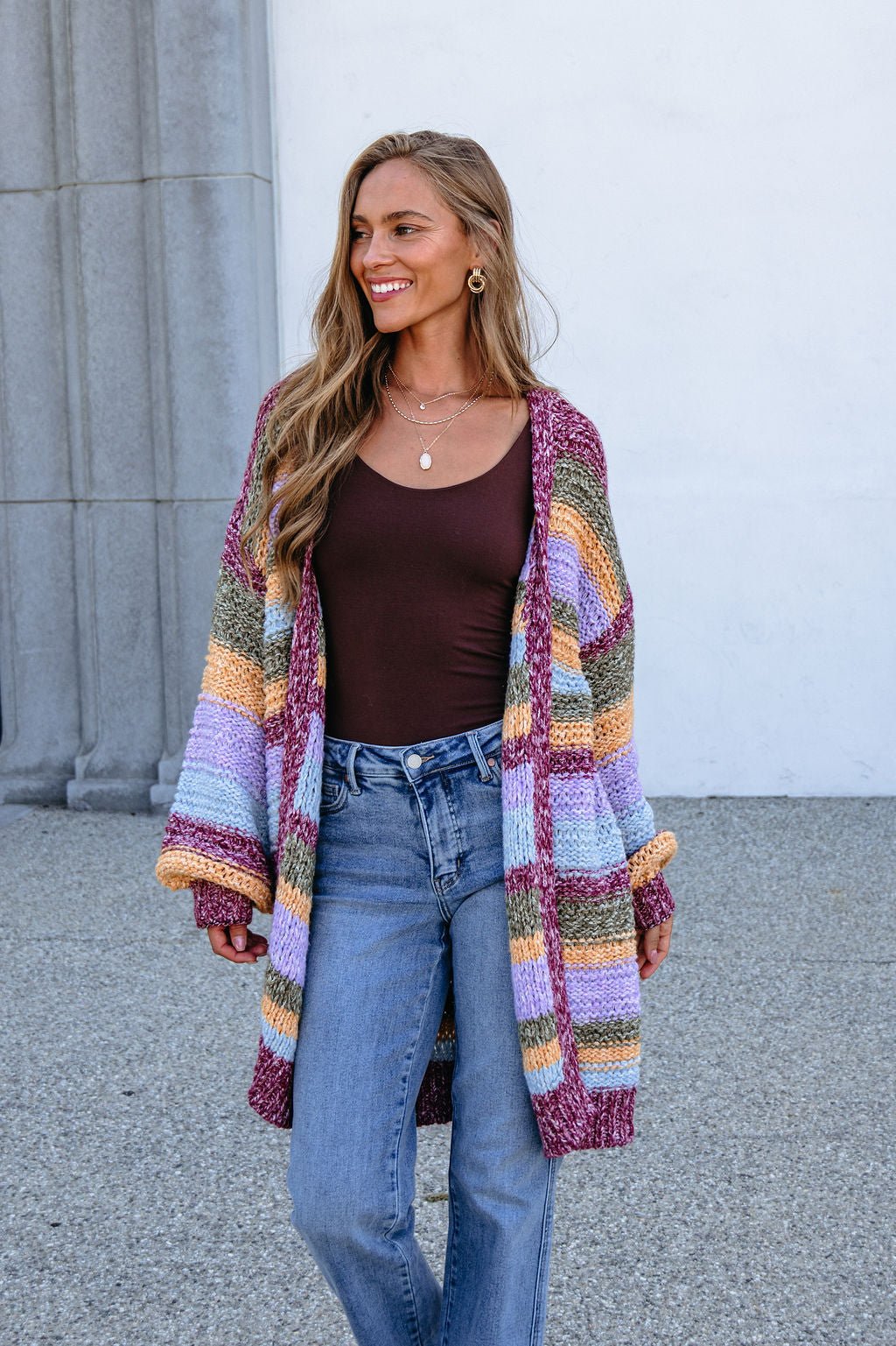 Woman smiles outdoors in a Burgundy Striped Open Front Cardigan and blue jeans. Bump-friendly.