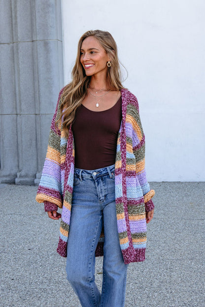 Woman smiles outdoors in a Burgundy Striped Open Front Cardigan and blue jeans. Bump-friendly.