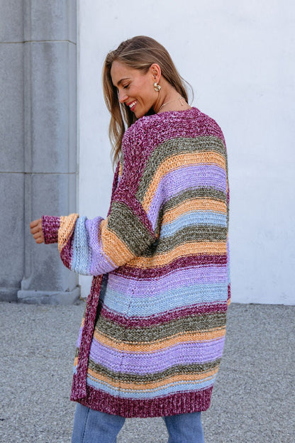 A woman smiles sideways outdoors by a gray column in a Burgundy Striped Open Front Cardigan.