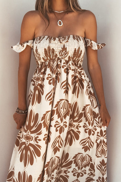 Woman in the Calista Print Off The Shoulder Maxi Dress - Taupe with ruffled sleeves, smocked bodice, floral print, and jewelry.