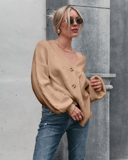 Woman wearing sunglasses and Camden Button Down Cardigan - Taupe with blue jeans stands against a stone wall, looking to the side.