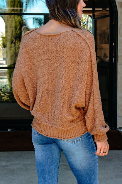 A woman in a Camel Boat Neck Seam Detail Sweater and blue jeans stands outdoors, her back to the camera.