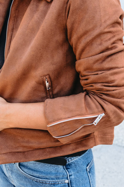 A person outdoors wearing a Camel Suede Zip Up Jacket with silver zippers and blue jeans.
