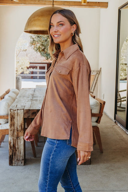 Smiling woman stands indoors in a Carmel Brown Faux Suede Shacket and blue jeans, an ideal fall layering piece.