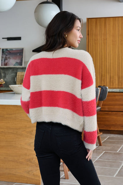 A woman wearing the Carmen Red and Taupe Striped Sweater and black jeans stands in a modern kitchen, facing away.
