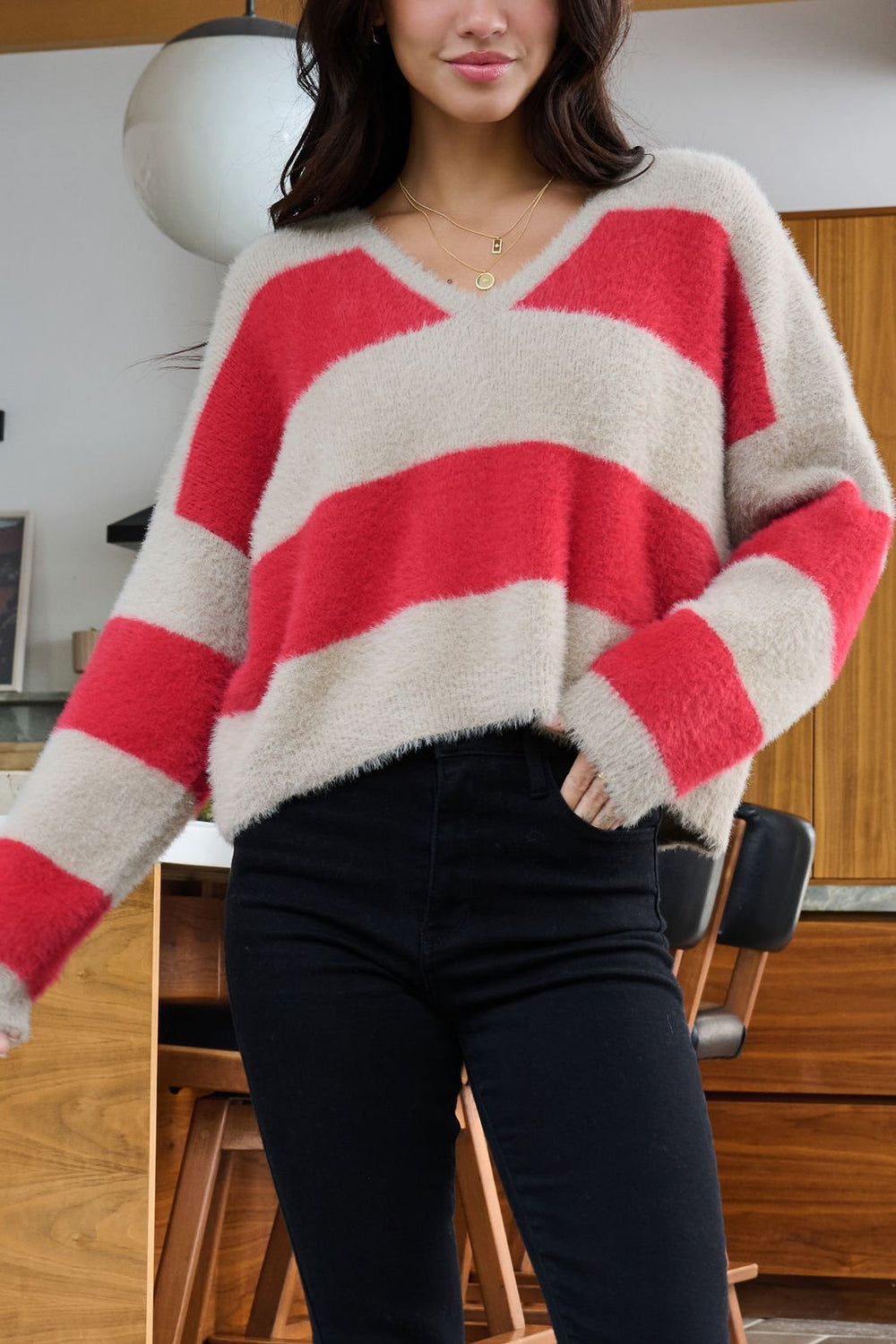Woman wearing the Carmen Red and Taupe Striped Sweater with a V neckline and black jeans in a modern kitchen.