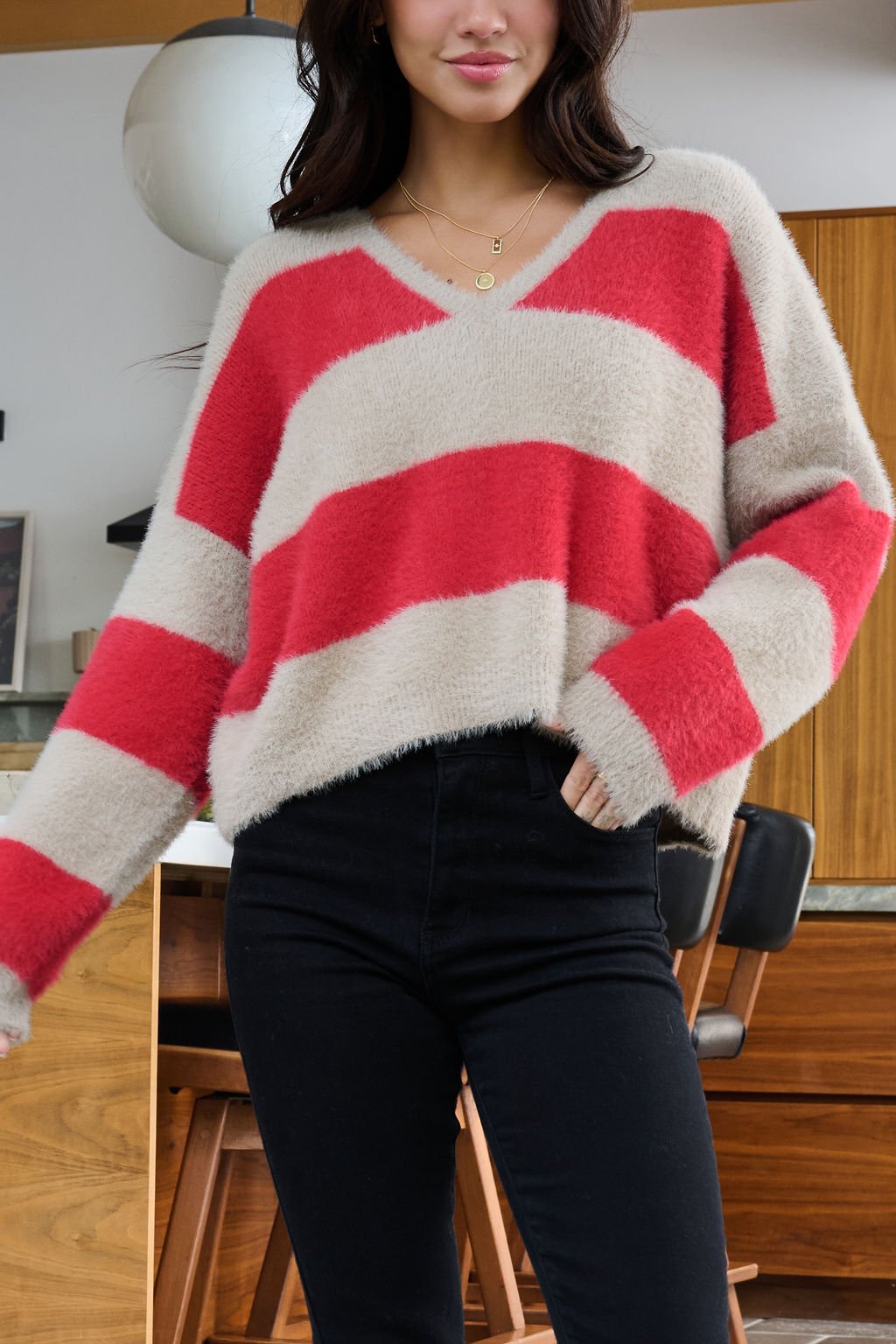 Woman wearing the Carmen Red and Taupe Striped Sweater with a V neckline and black jeans in a modern kitchen.
