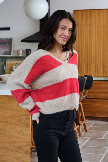 Woman in the Carmen Red and Taupe Striped Sweater with a V neck and black jeans, standing in a modern kitchen with wooden cabinets.