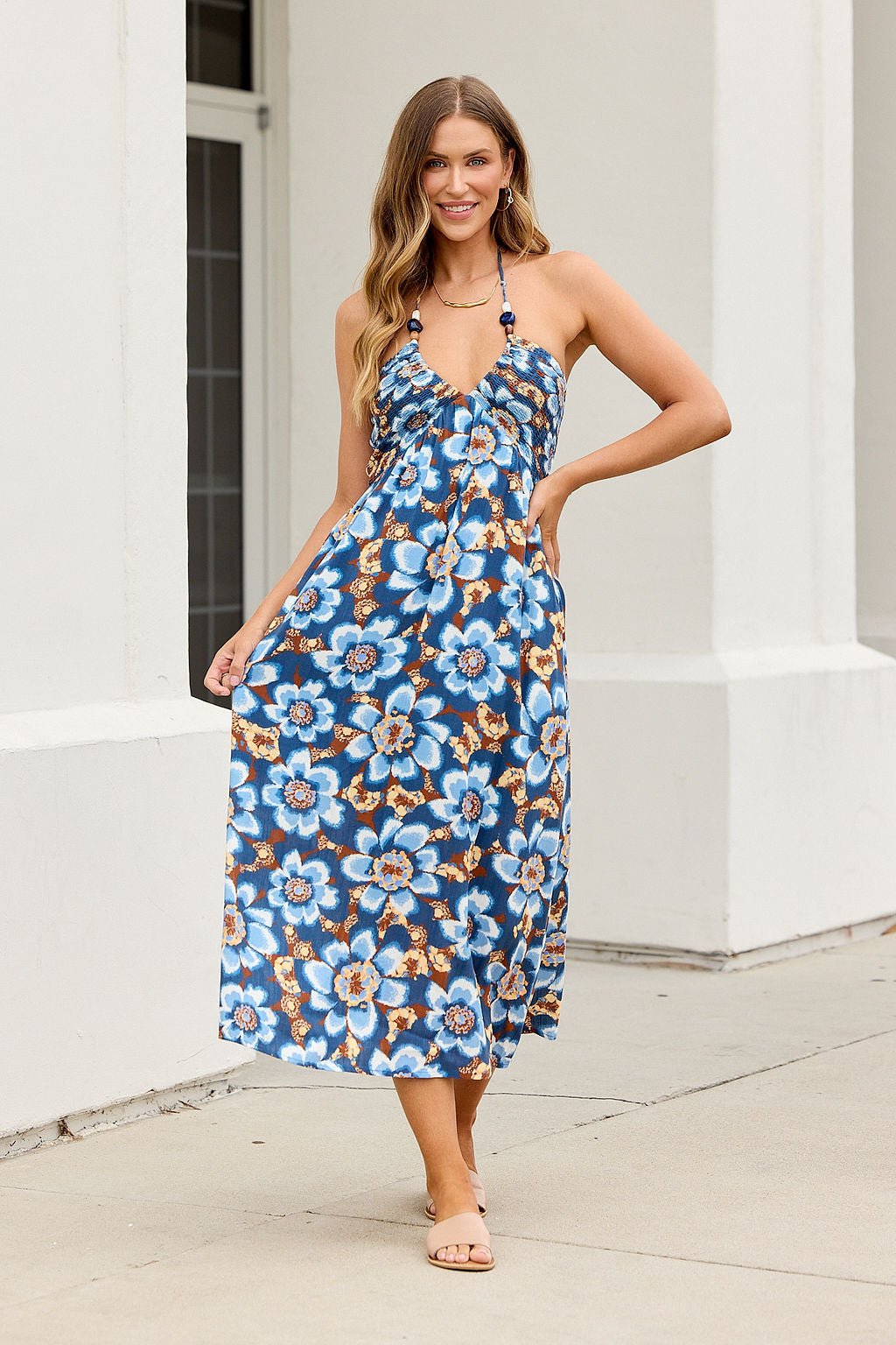 Woman wears the Catalina Halter Midi Dress - Navy as she smiles outdoors, one hand on her hip, the other holding her dress.
