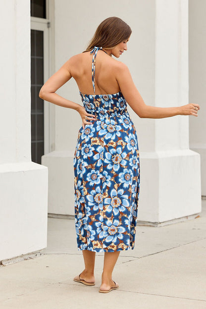 Woman in the Catalina Halter Midi Dress - Navy and sandals stands outdoors by white columns, facing away from the camera.