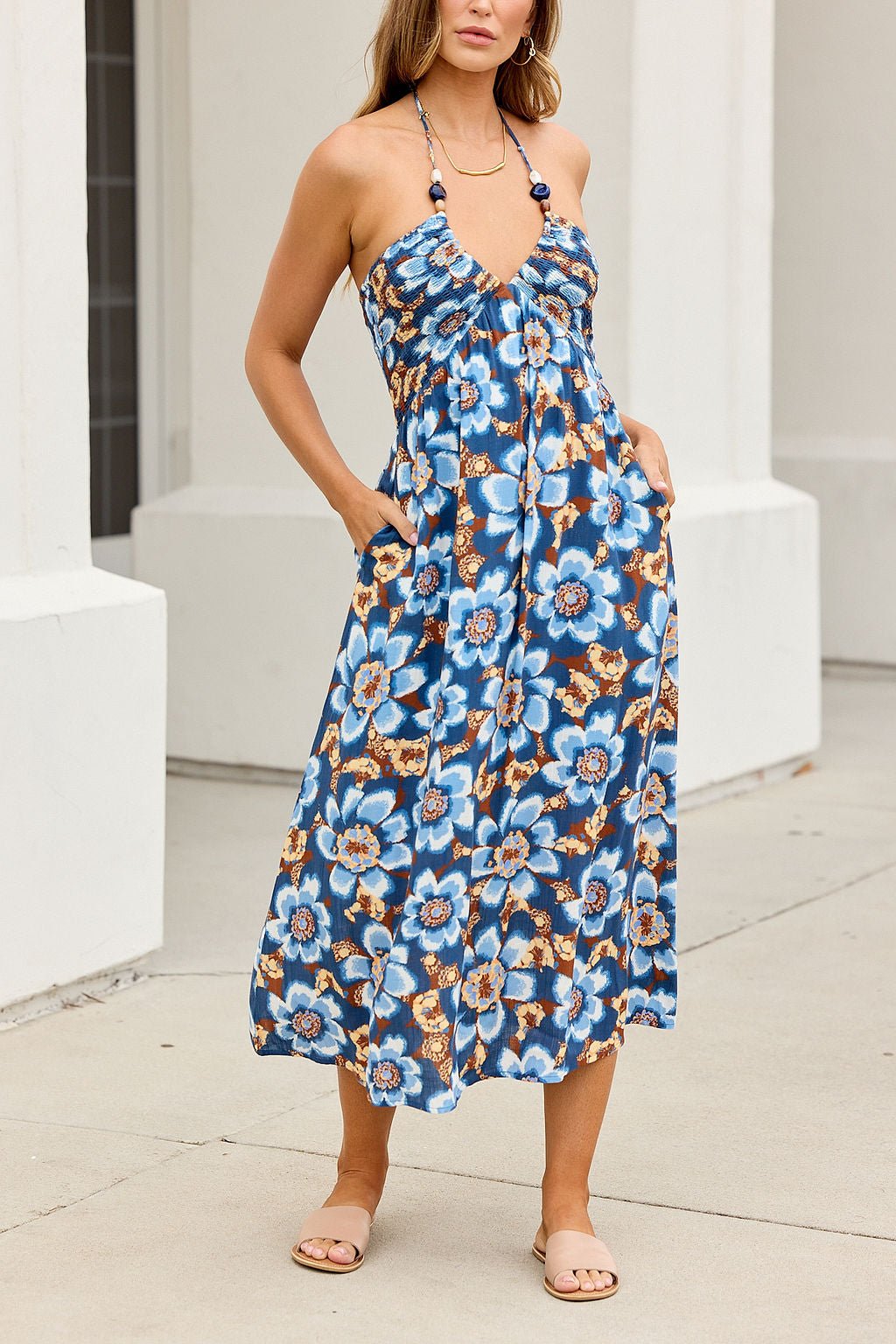 Woman in a Catalina Halter Midi Dress - Navy, standing outdoors on a sidewalk, wearing tan sandals.