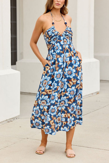 Woman in a Catalina Halter Midi Dress - Navy, standing outdoors on a sidewalk, wearing tan sandals.