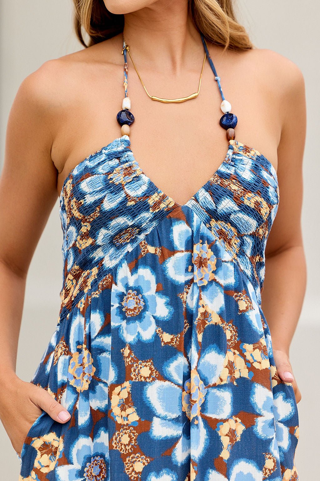 Woman wearing the Catalina Halter Midi Dress - Navy with a shirred bodice, gold necklace, and hands in pockets.