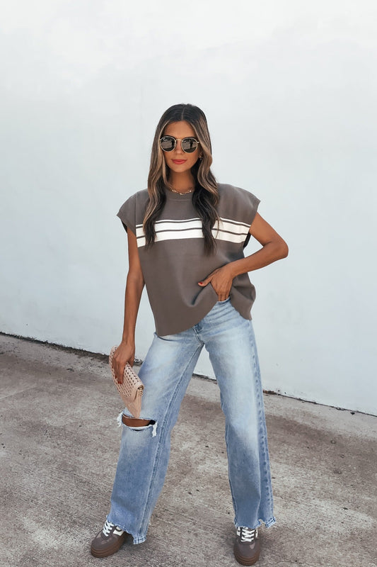 Woman in sunglasses poses in a relaxed fit Catalina Striped Top - Olive with ripped jeans, holding a woven clutch.