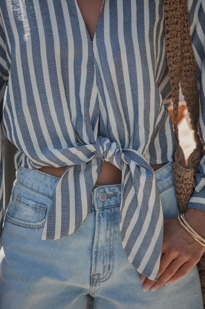 Wearing a Chambray Striped Tie Knot Shirt, light denim jeans, and carrying a woven bag.