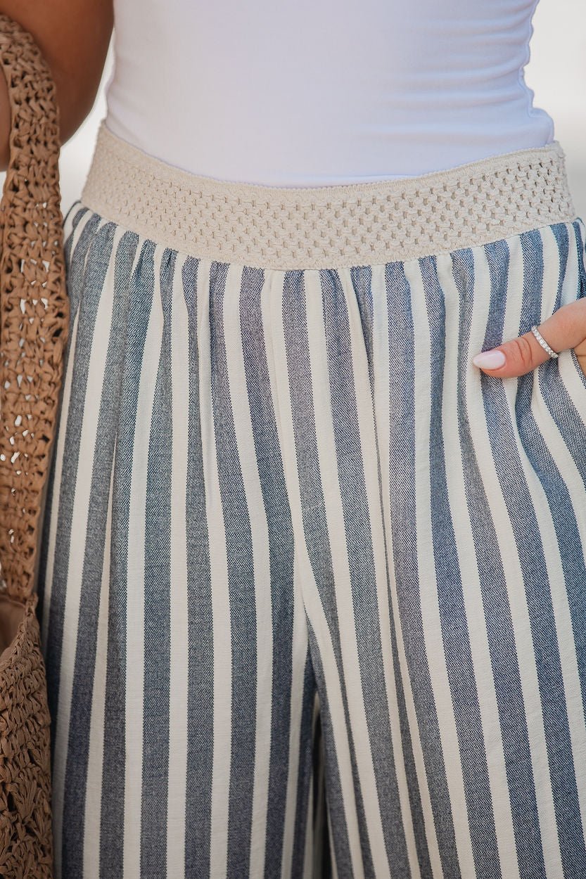 Woman wears Chambray Striped Wide Leg Pants with a crocheted waistband, holding a woven bag and displaying manicured nails.