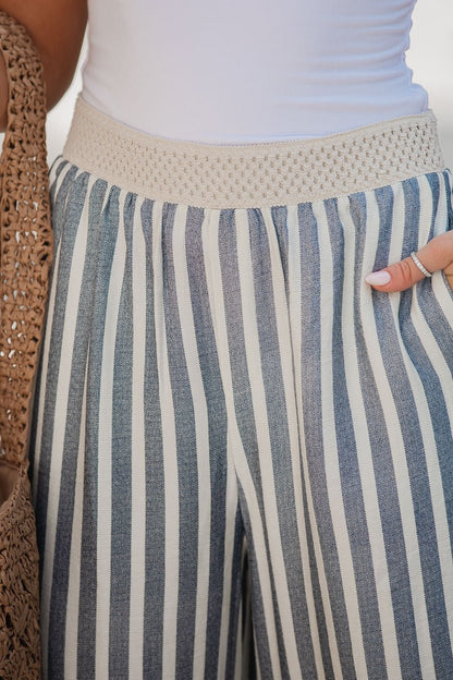 Woman wears Chambray Striped Wide Leg Pants with a crocheted waistband, holding a woven bag and displaying manicured nails.