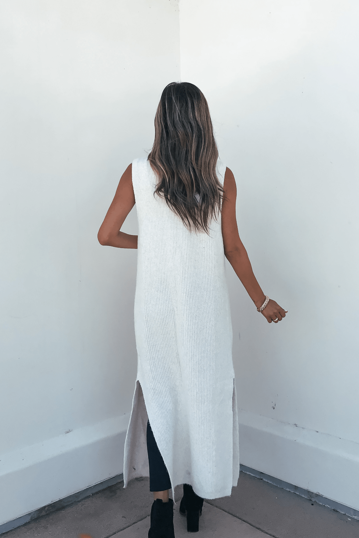 A woman with wavy hair wears the Champagne Open Front Long Cardigan, her perfect fall layering piece by a white wall.