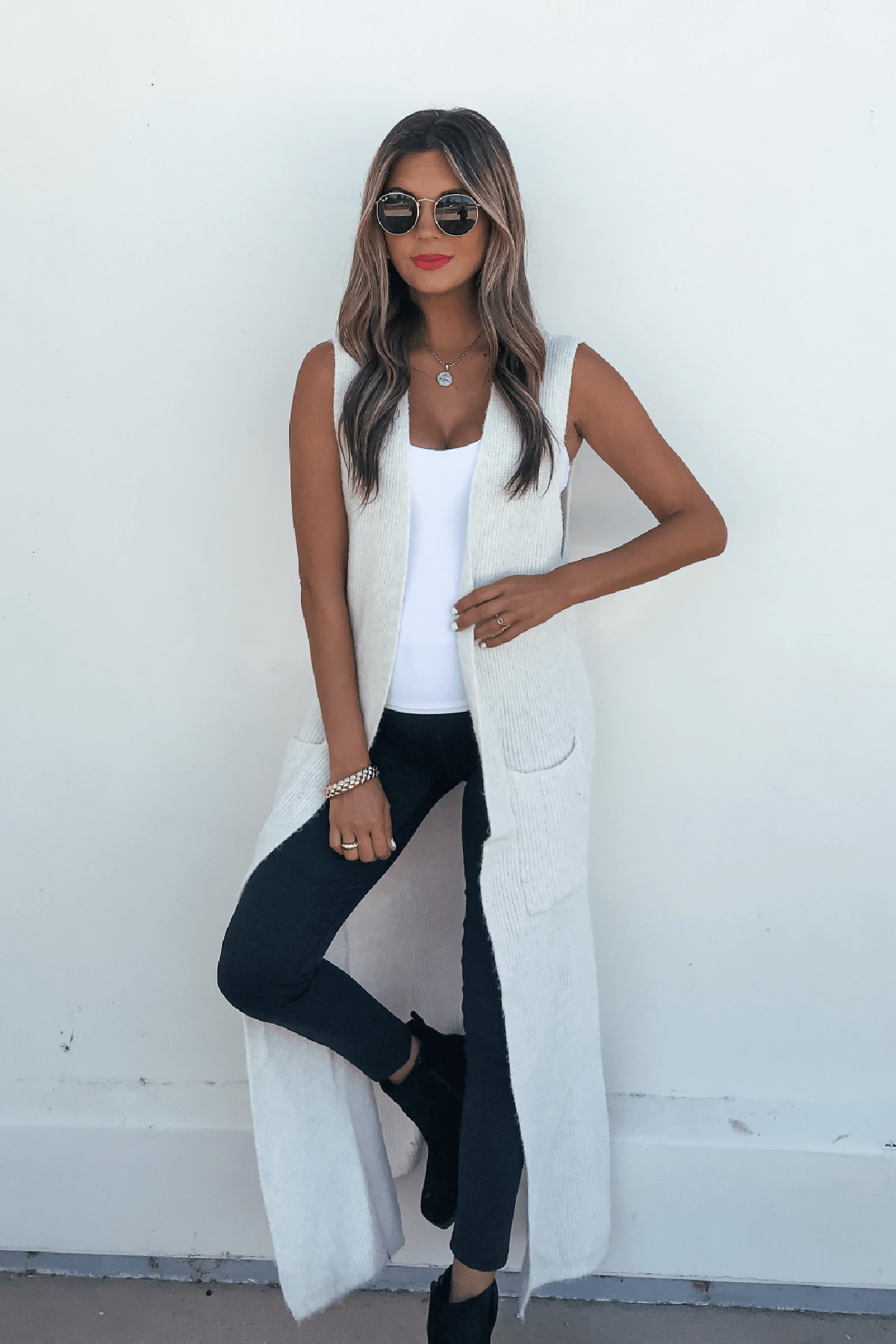 Woman in sunglasses and black pants models the Champagne Open Front Long Cardigan, a chic fall staple, against a white wall.