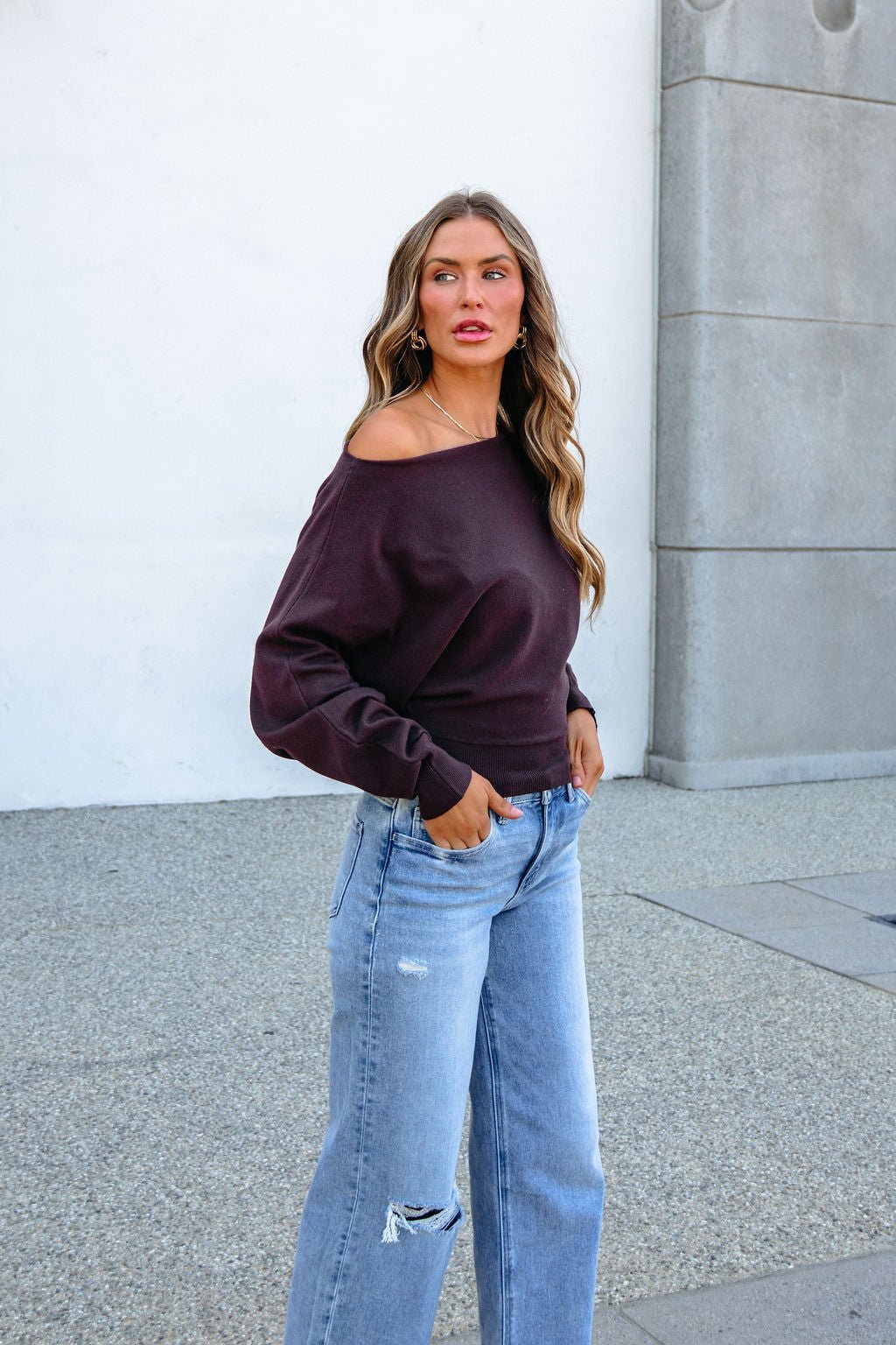 A woman wearing a CHARLOTTE AVERY COFFEE BOATNECK CASHMERE SWEATER and light blue wide-leg jeans.