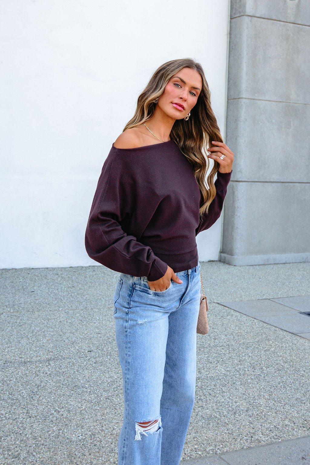 A woman wearing a CHARLOTTE AVERY COFFEE BOATNECK CASHMERE SWEATER and light-wash distressed jeans.