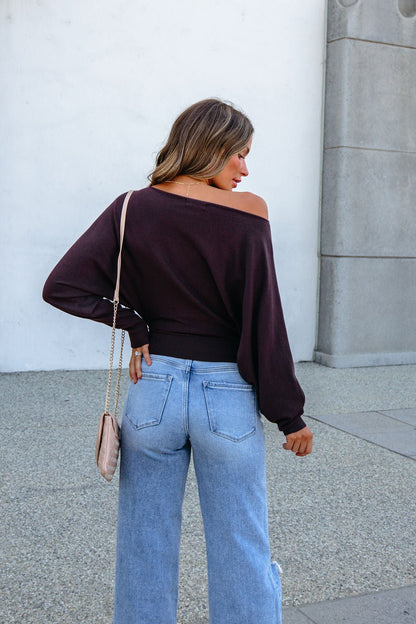A woman from behind wearing a CHARLOTTE AVERY COFFEE BOATNECK CASHMERE SWEATER, light wash wide-leg jeans, and a crossbody bag.