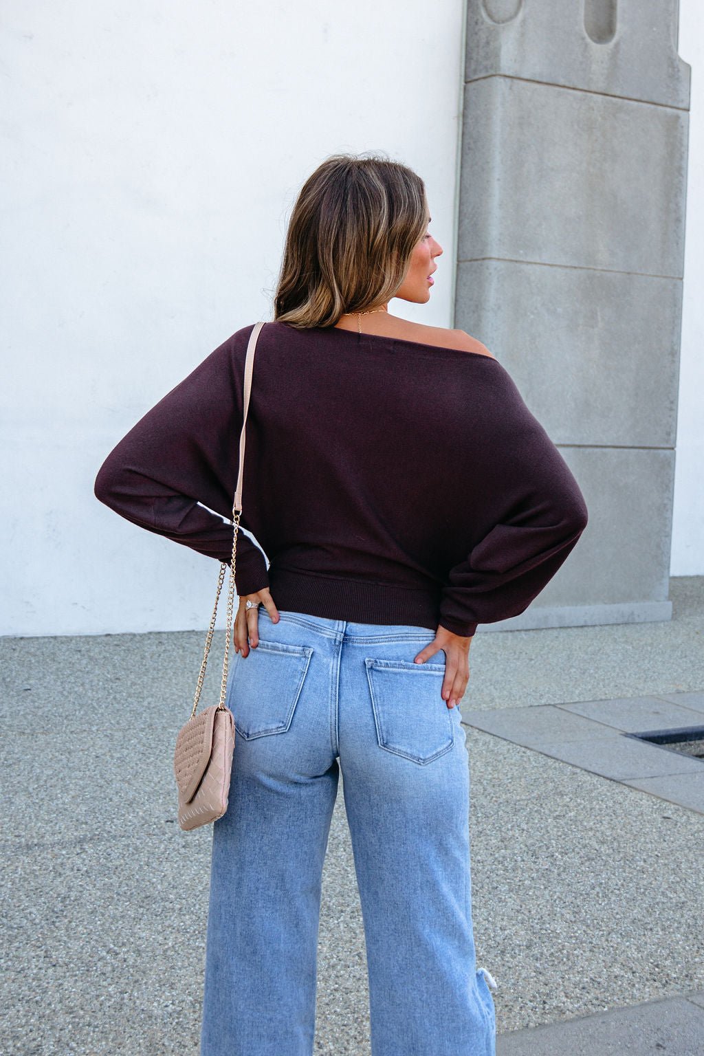 A woman wearing a CHARLOTTE AVERY COFFEE BOATNECK CASHMERE SWEATER and light-wash blue jeans with a crossbody bag.