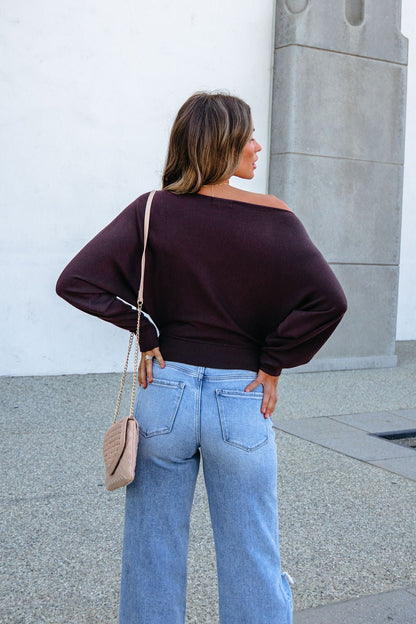 A woman wearing a CHARLOTTE AVERY COFFEE BOATNECK CASHMERE SWEATER and light-wash blue jeans with a crossbody bag.
